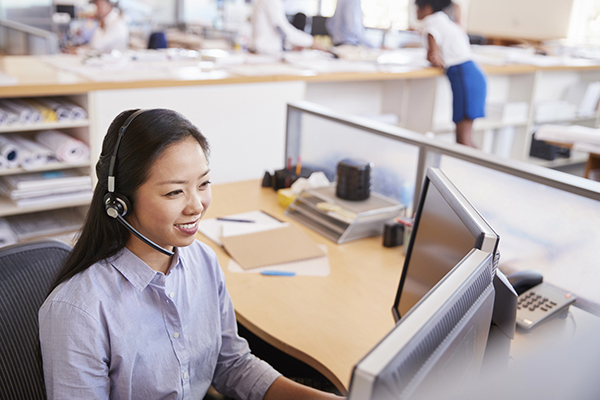 IT Support A professional woman providing IT Support in Tokyo, Japan, wearing a headset and working at her desk in a modern office environment
