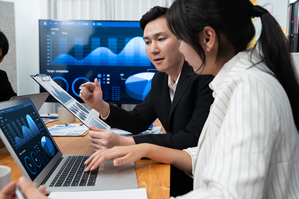Project Management Business professionals discussing Japan IT Project Management, analyzing data charts on a laptop and presentation screen in an office