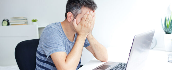 Man's hand on his face due to his laptop restarted unexpectedly which is one of the most common computer problems.