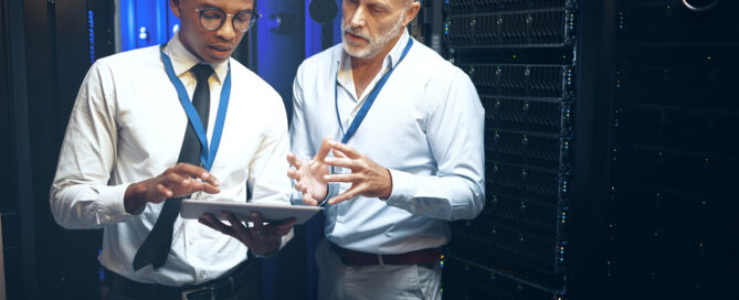 Two IT professionals discuss a tablet in a server room, highlighting collaboration in outsourcing IT services.
